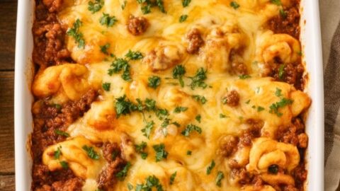 Cheesy Beef Enchiladas Tortellini Recipe in a white ceramic dish with melted cheese, rich red enchilada sauce, seasoned ground beef, and fresh cilantro garnish on a wooden table.